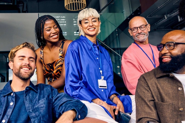 Six men and woman of different ages and ethnicities sit together mostly looking at the camera